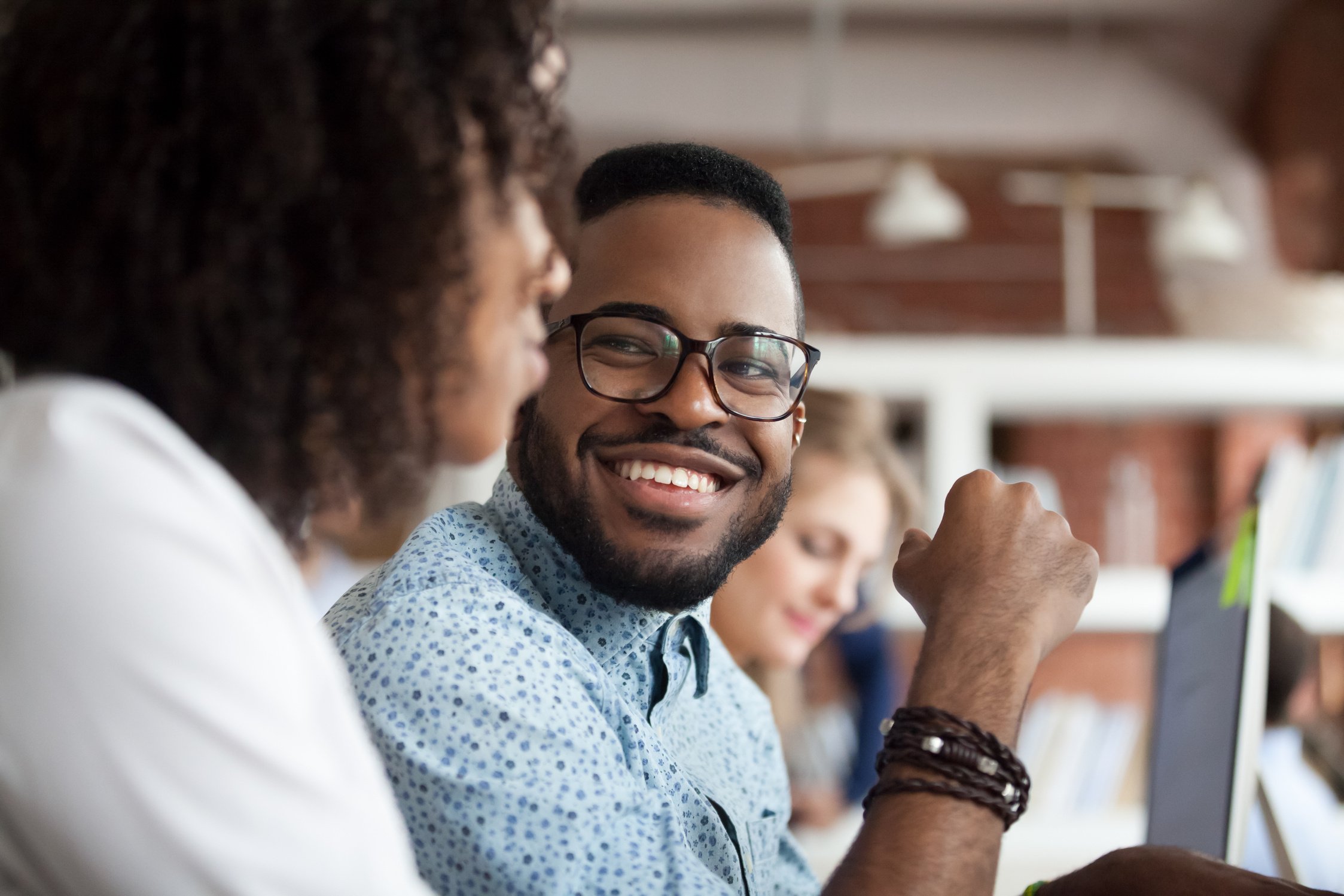 Smiling African American male employee look at colleague chatting