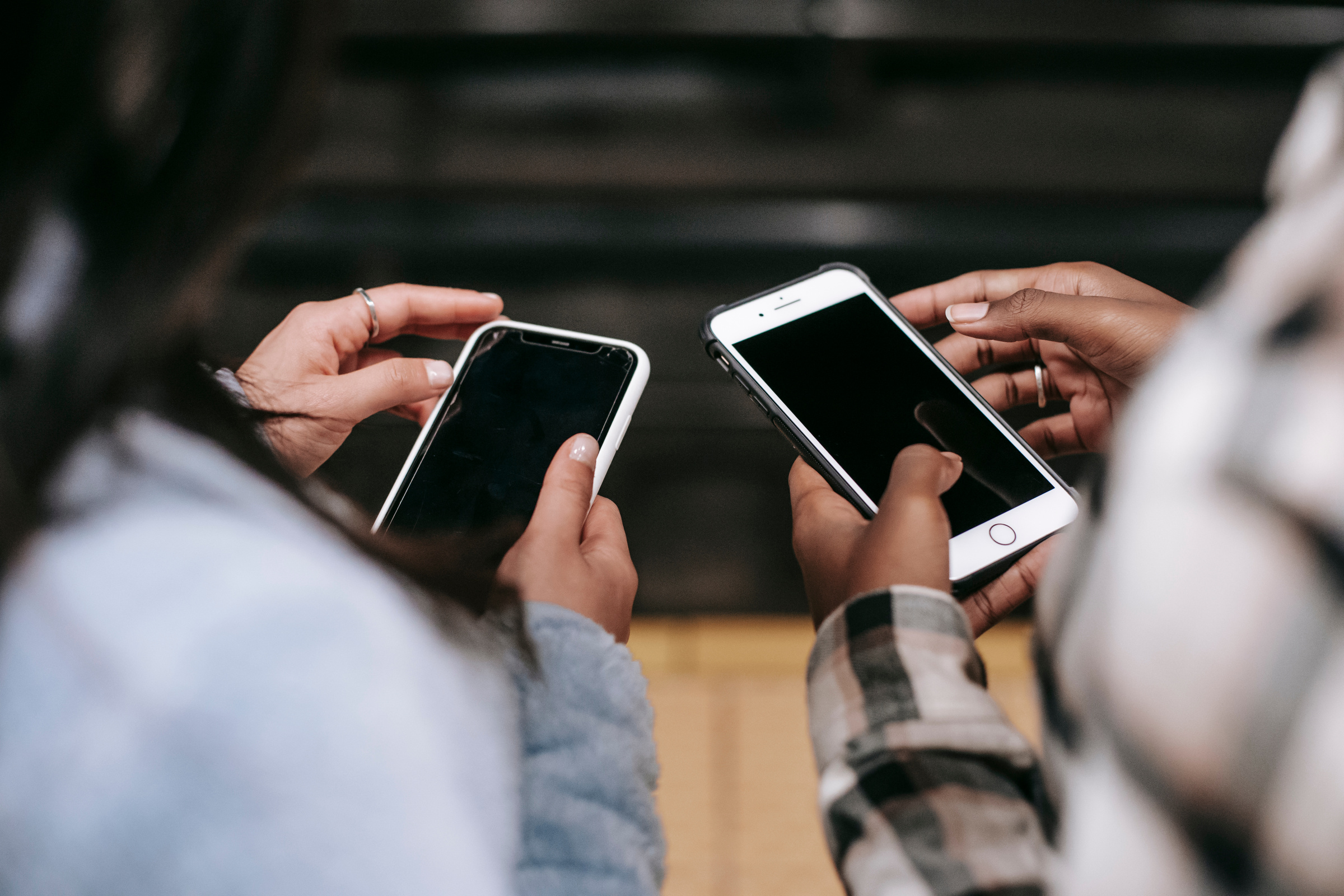 Crop diverse female partners chatting on smartphones with black screens